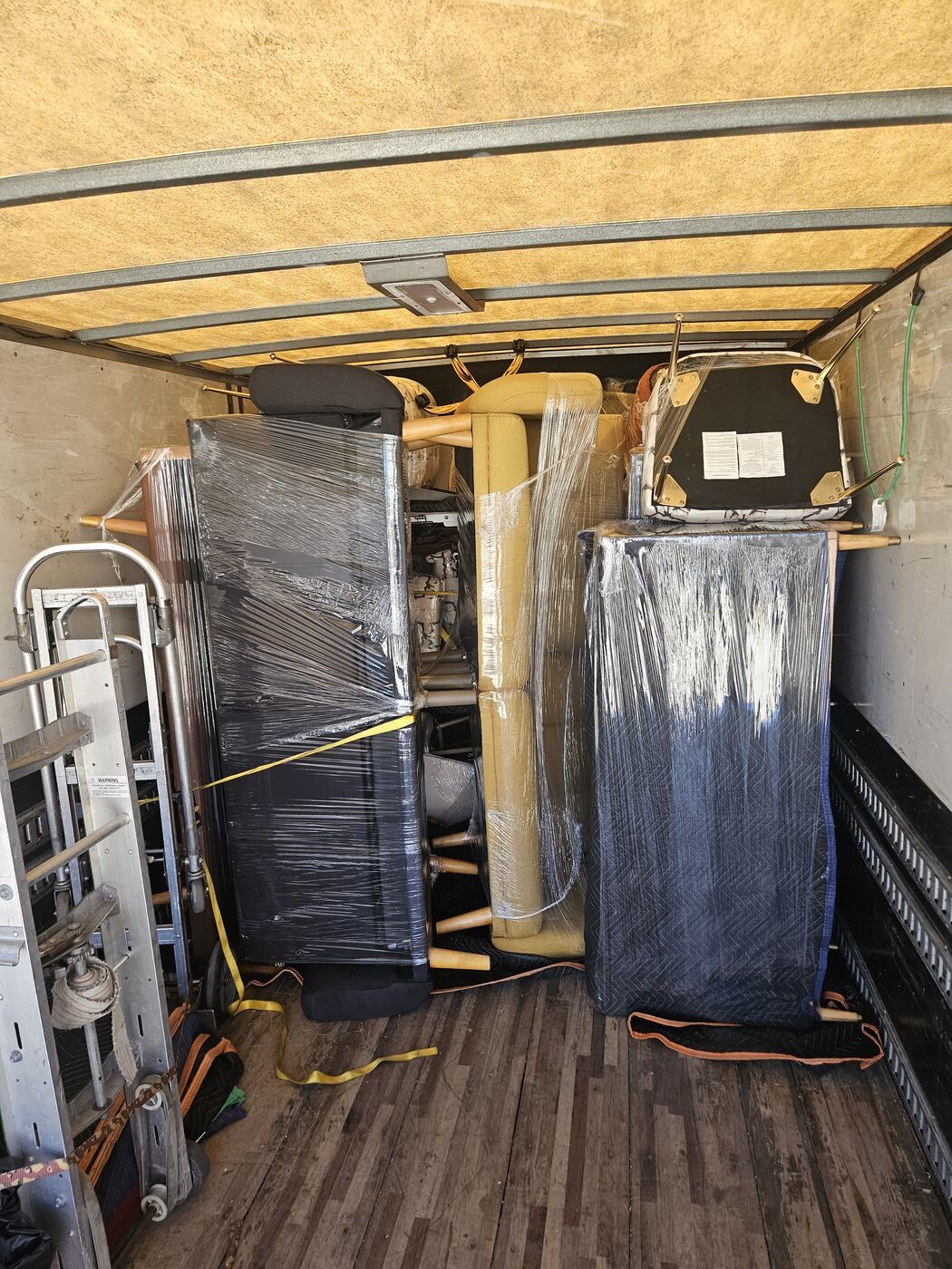 Shrink-wrapped dresser and mattress stood upright and strapped inside a box truck
