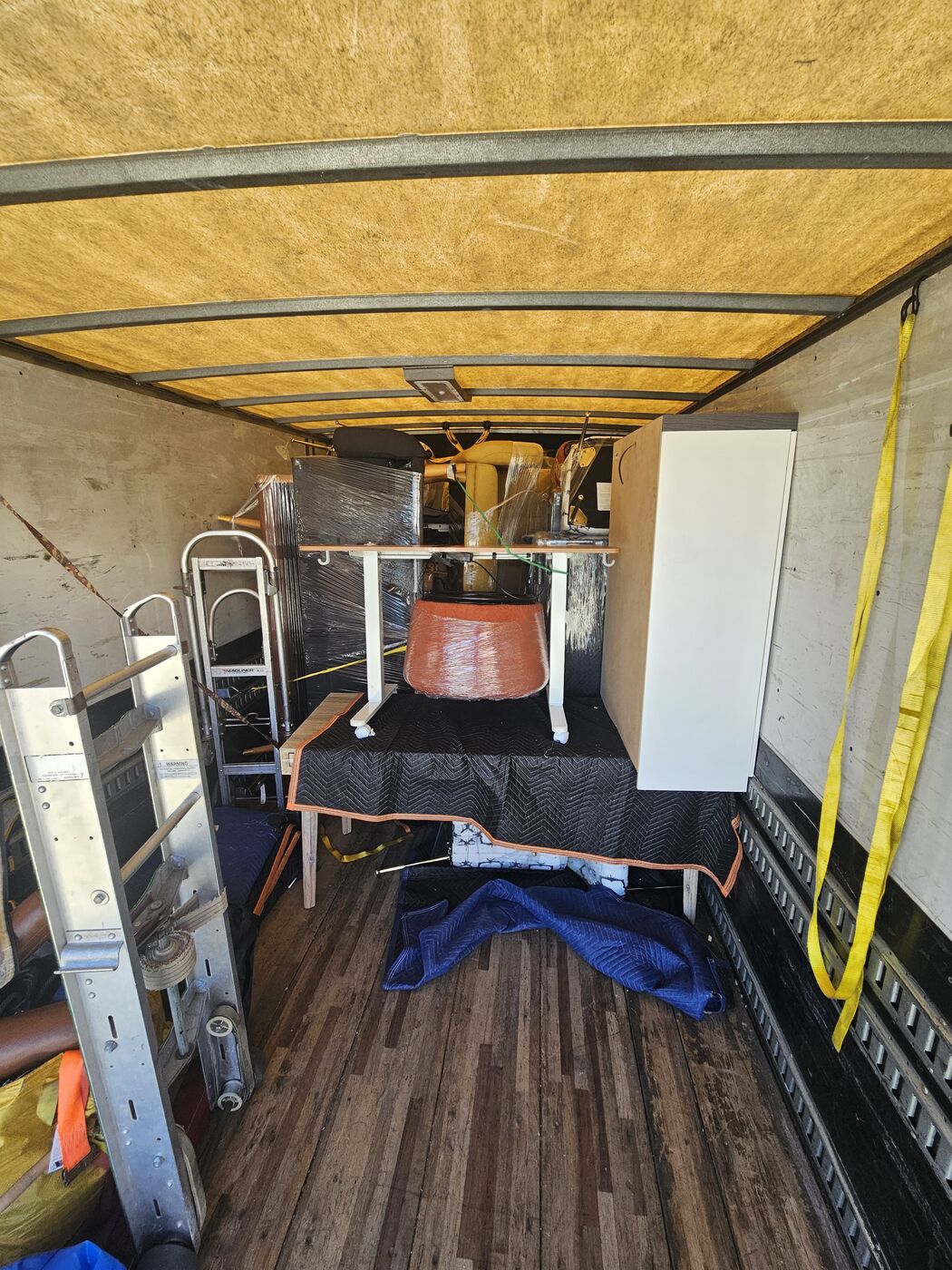 Professional packer building the first tier of a box truck load with blanket-wrapped furniture